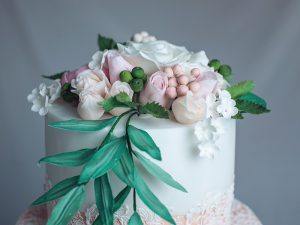 A beautiful spring two-tiered cake decorated with roses from mastic top and ornament around. Concept confectionery floristics. Food design. trends