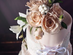 Beautiful three-tiered wedding cake in the form of dresses with lace and ribbon in a corset decorated with flowers and roses on top. The concept of unusual wedding desserts