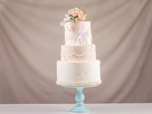 A large tiered wedding cake in the form of dress with lace decorated with pink roses on top of the table. The concept of festive desserts