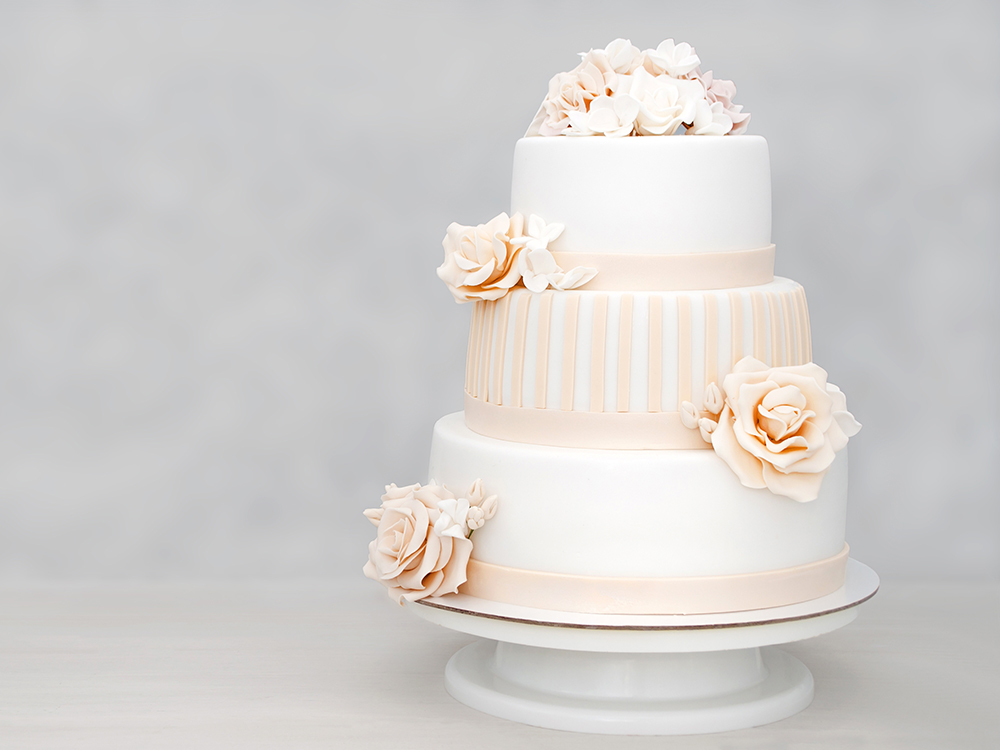 Three-tiered white wedding cake decorated with flowers from mast